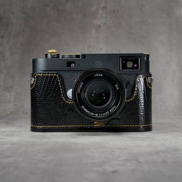 Leica M11 in a black gloss lizard FlexCase with gold stitching, front view on a grey studio backdrop