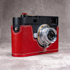 Leica M11 in a Ruby Gloss FlexCase with an OxBlood plate, three quarter front view on a grey studio backdrop