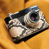 Leica M11 in a Python FlexCase with a brass base plate, resting on mustard leather