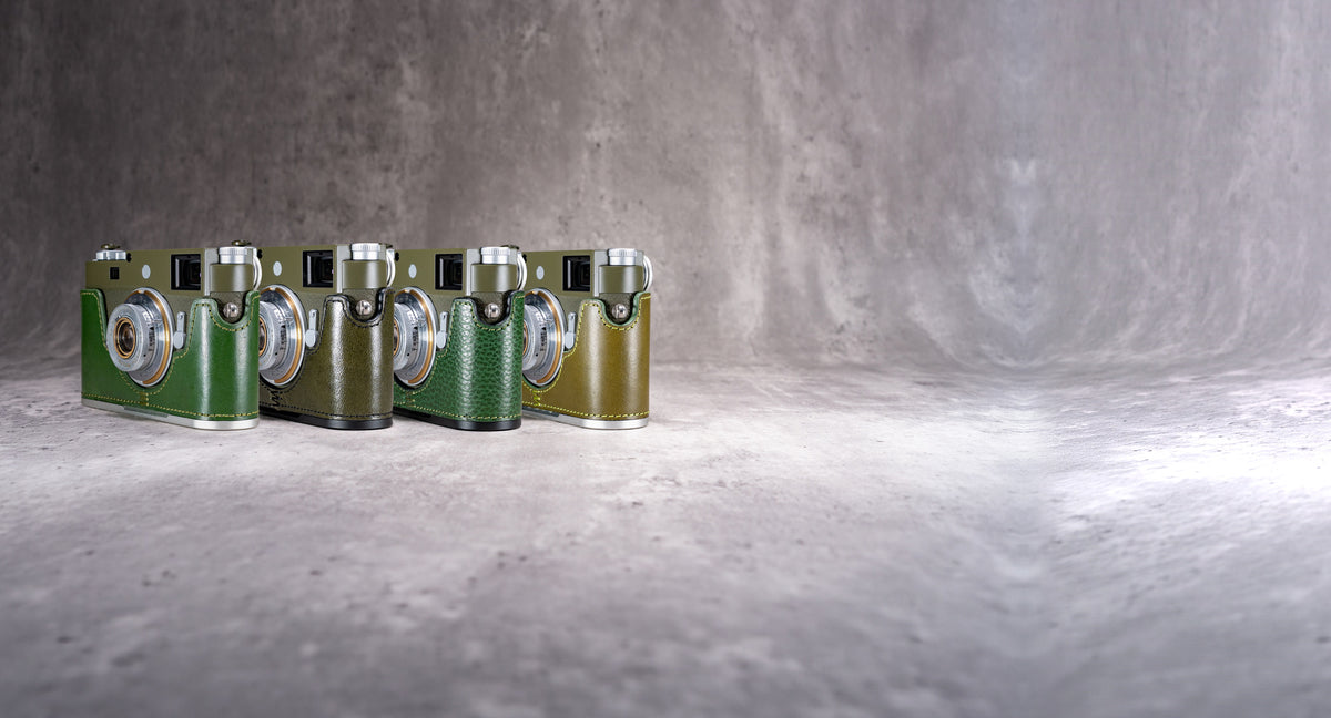 Four FlexCases in green leather on Leica M bodies, standing in a row on concrete