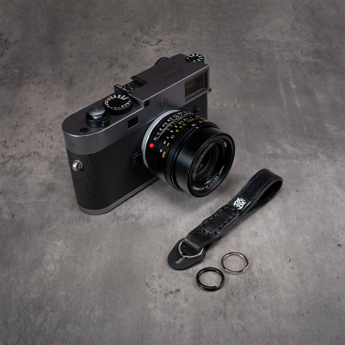 Leather Thumb Strap - Stealth beside a Leica M camera with black and polished split rings