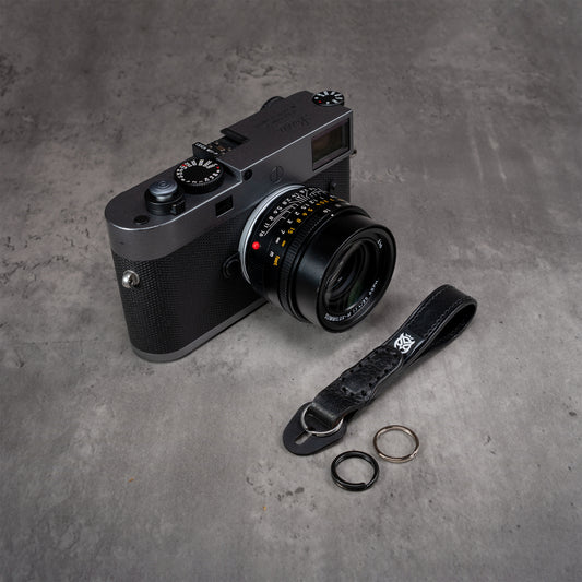 Leather Thumb Strap - Stealth beside a Leica M camera with black and polished split rings