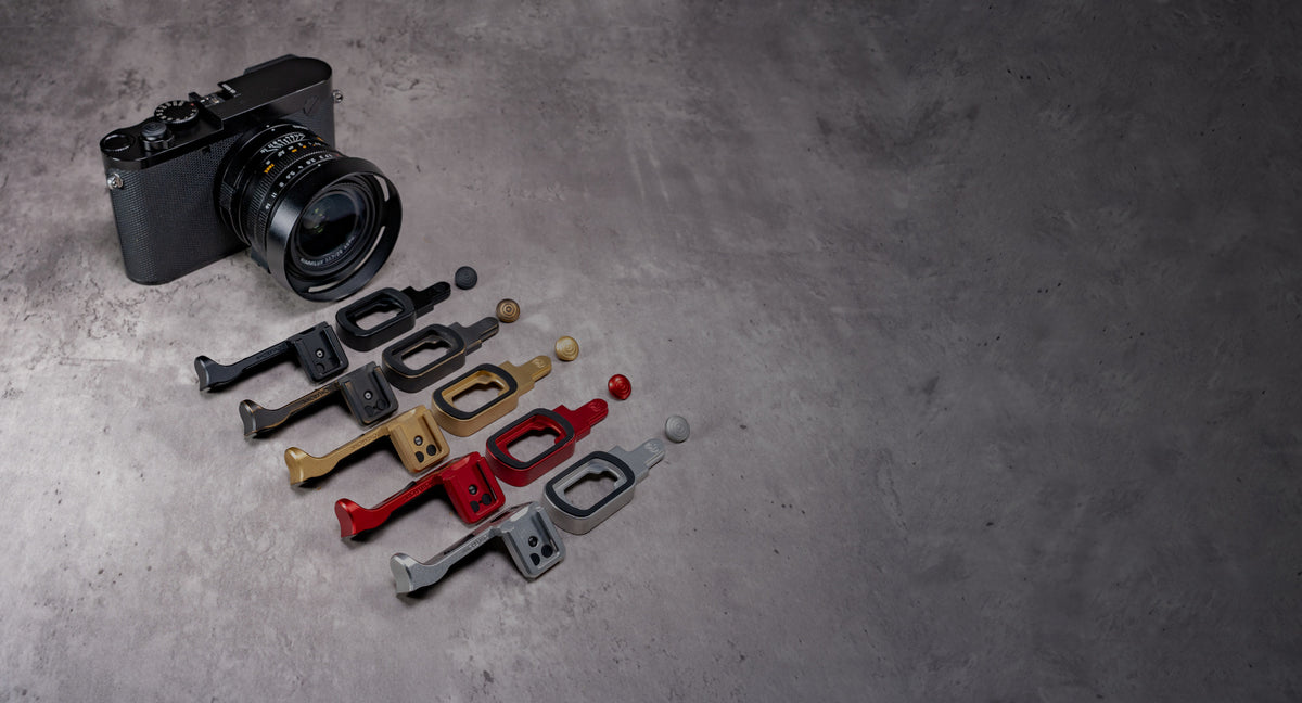 The Leica Q with five ProKits laid out beside it in Black Chrome, Black Patina, Solid Brass, OxBlood and Silver Chrome